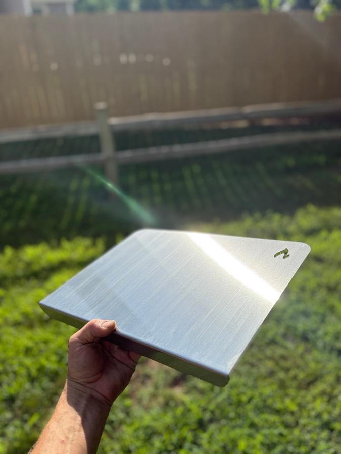 A hand holding a STELE Medium board outdoors in sunlight, showing the solid steel edge